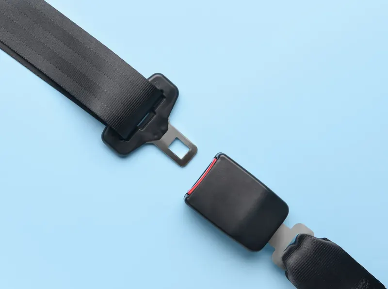 A seat belt assembly photographed flat: webbing with a latch plate on one side and the buckle receiver with its own webbing stalk on the other.