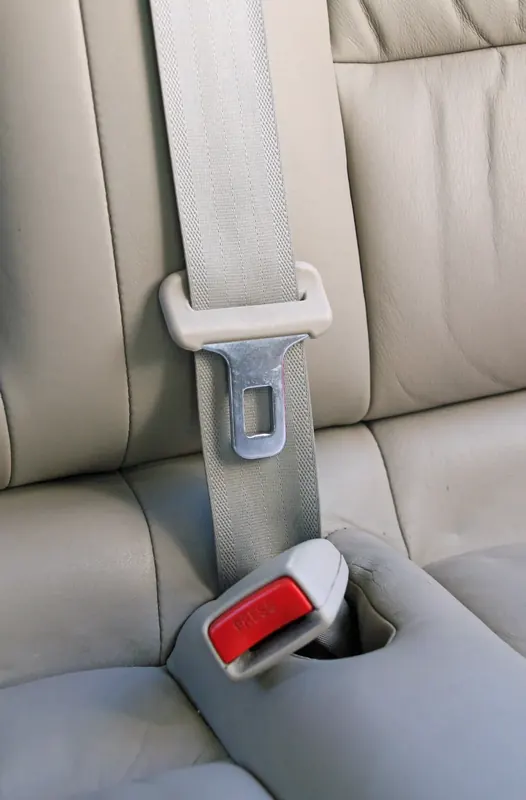 A three-point seat belt fitted in a light-coloured vehicle interior, the webbing running from the shoulder down to a buckle set into the seat.