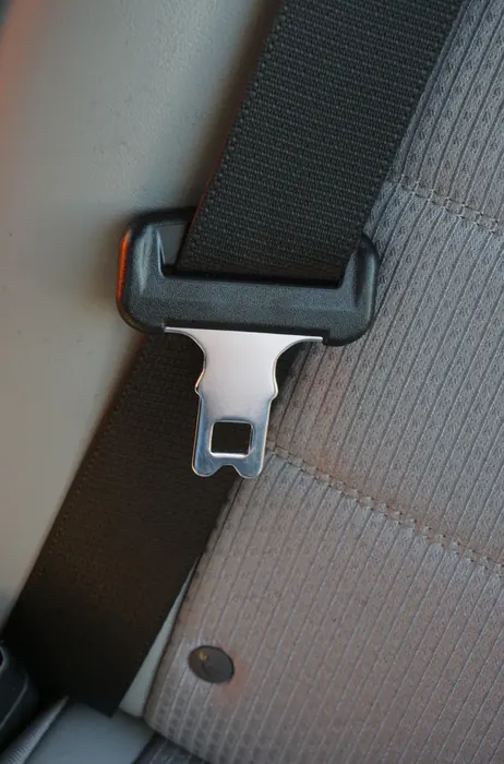 A seat belt latch plate and webbing resting on a vehicle seat, photographed close for inspection of the metal tongue and moulded housing.